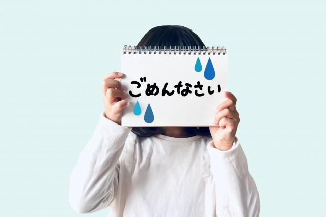 ごめんなさいと画用紙に書いて顔を隠す女の子